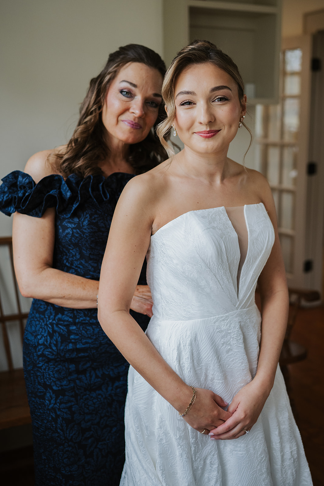 Mother of the bride assisting the bride as she stands in her wedding gown.