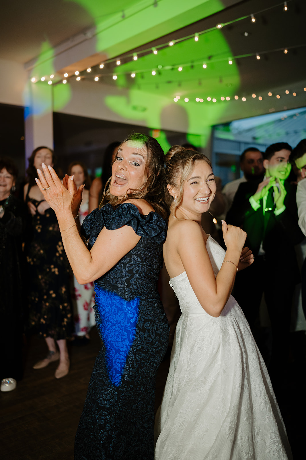 Bride laughing and dancing back-to-back with a guest on the lit-up reception dance floor.