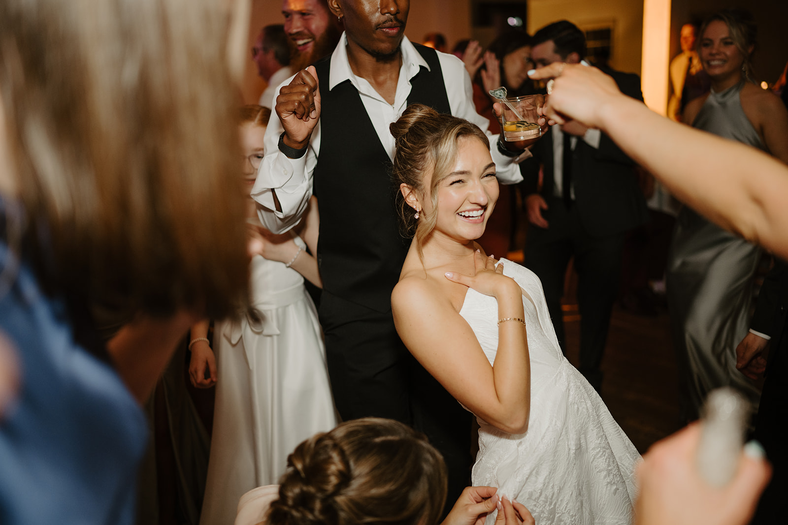 Color photo of the bride laughing and dancing in a crowd of guests during the late-night reception party at The Garrison.
