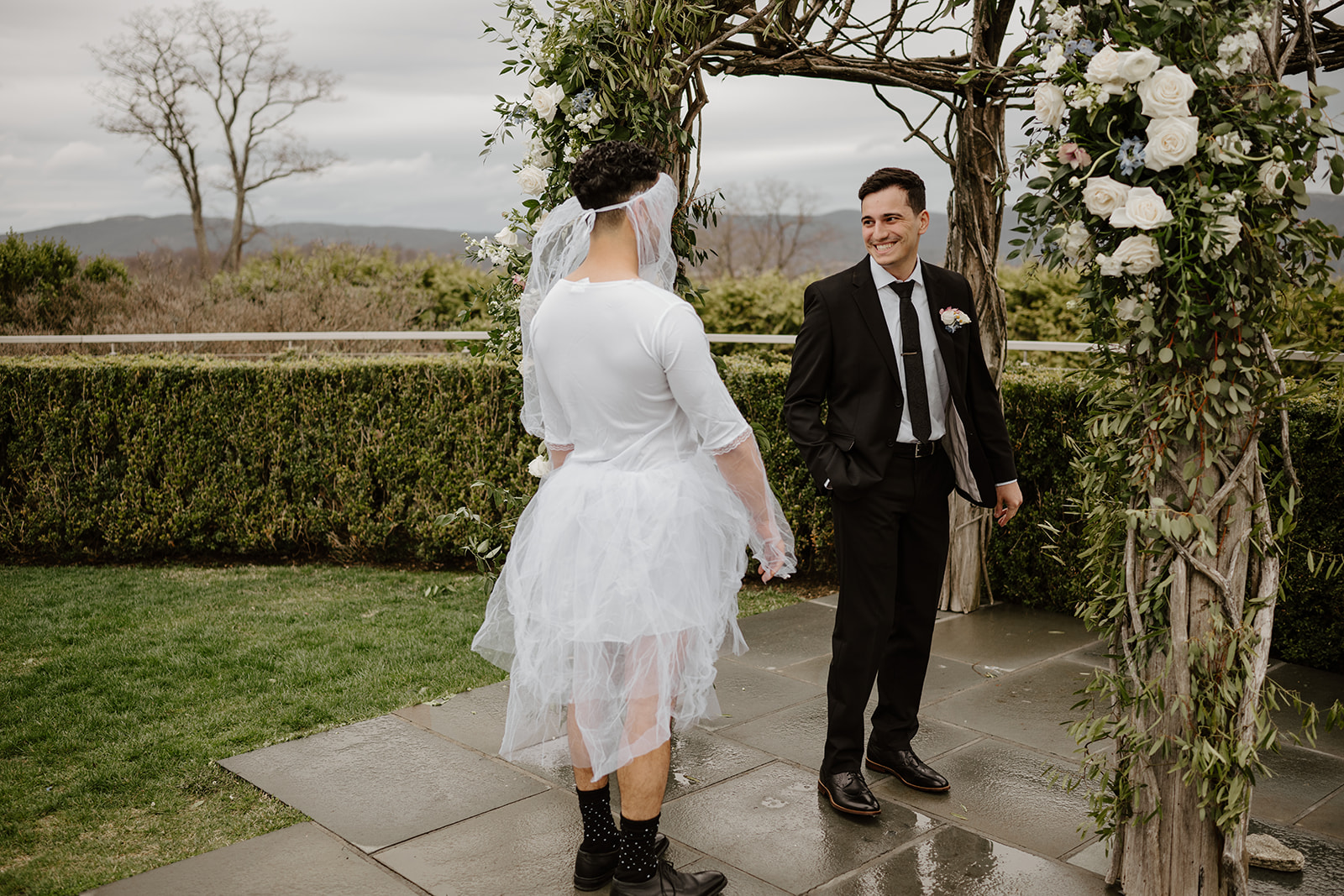 Groom turning around and smiling broadly as he sees the best man dressed in the white tutu/veil.