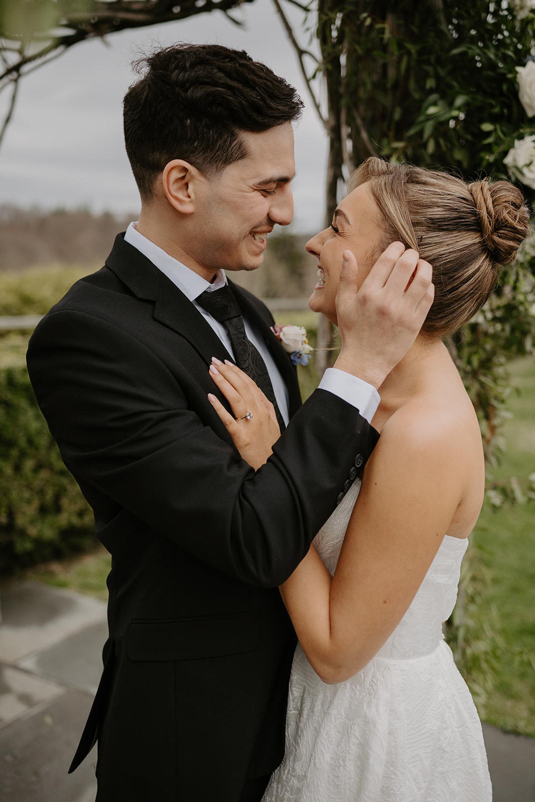 Close-up portrait of the bride under the wooden arch, touching her face and smiling.