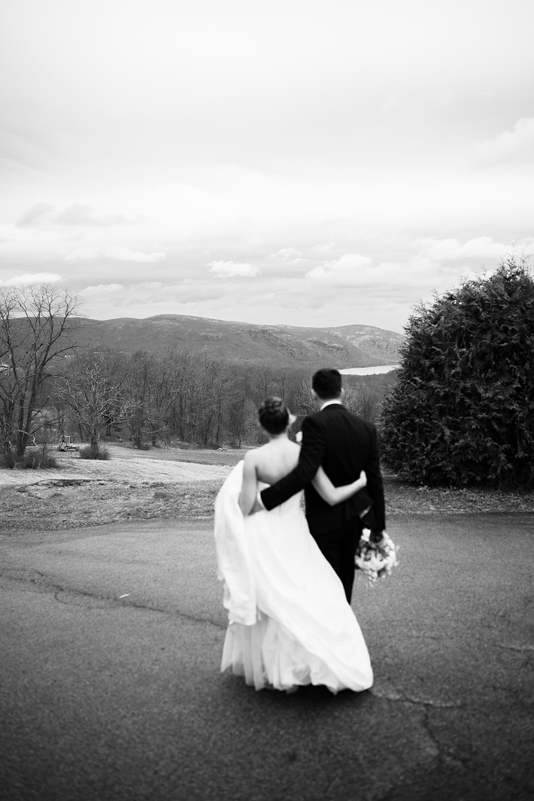 Black and white photo of the couple walking away, back view, overlooking the panoramic Hudson Highlands mountains.