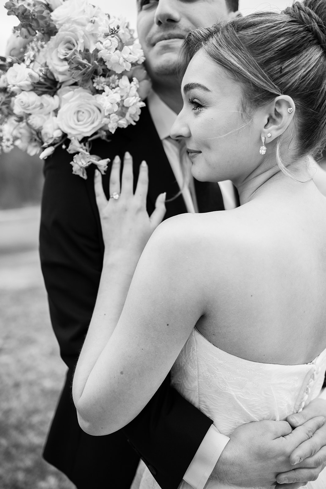 Close-up black and white photo of the bride's hand on the groom's chest showing her wedding ring.