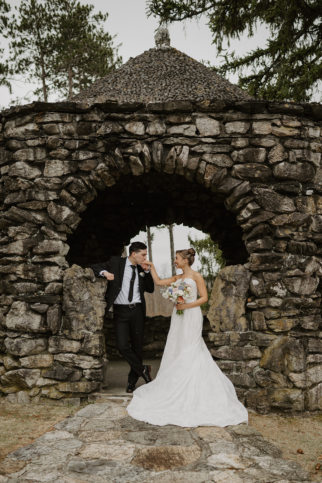 Groom kissing the bride's hand inside the rustic stone gazebo.