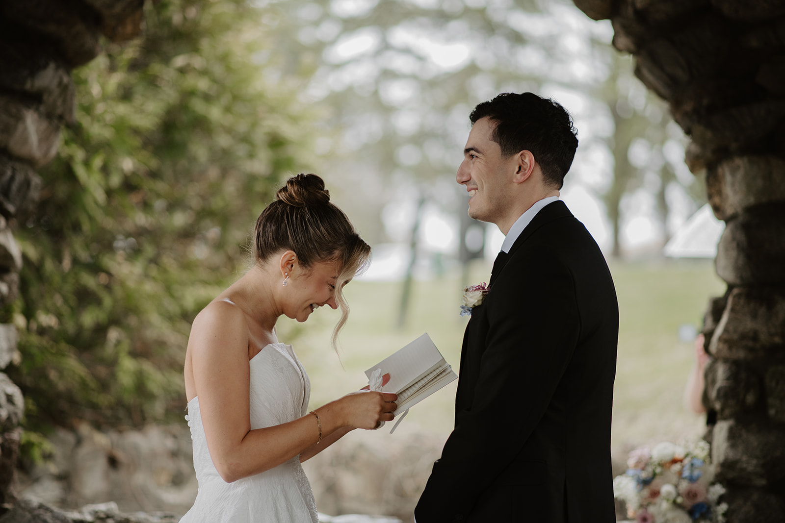 Bride reading private vows to the groom inside the stone gazebo, laughing.