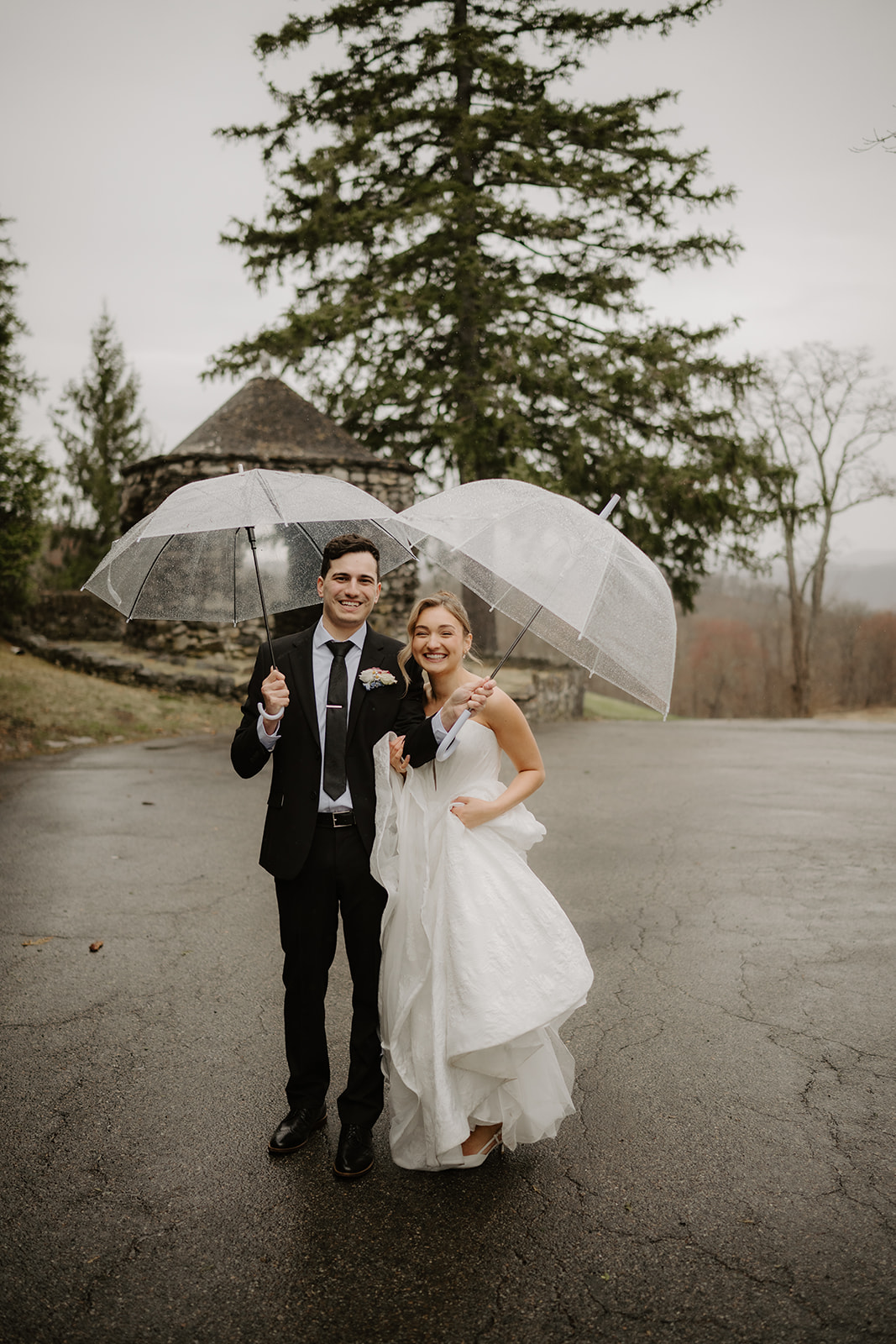 Couple standing together holding clear umbrellas on wet pavement, smiling.