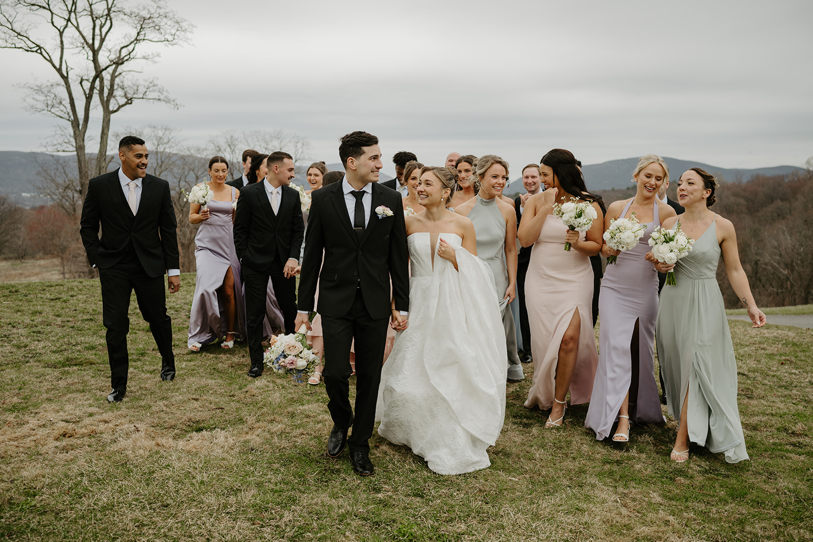 Couple walking hand-in-hand leading the wedding party across the lawn.