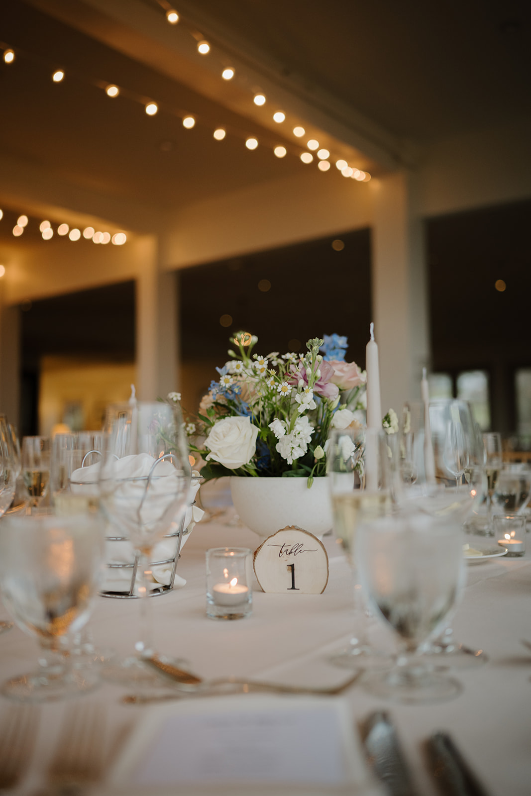 Detail of Table 1 setup, featuring a white floral centerpiece, candle, and custom place setting.