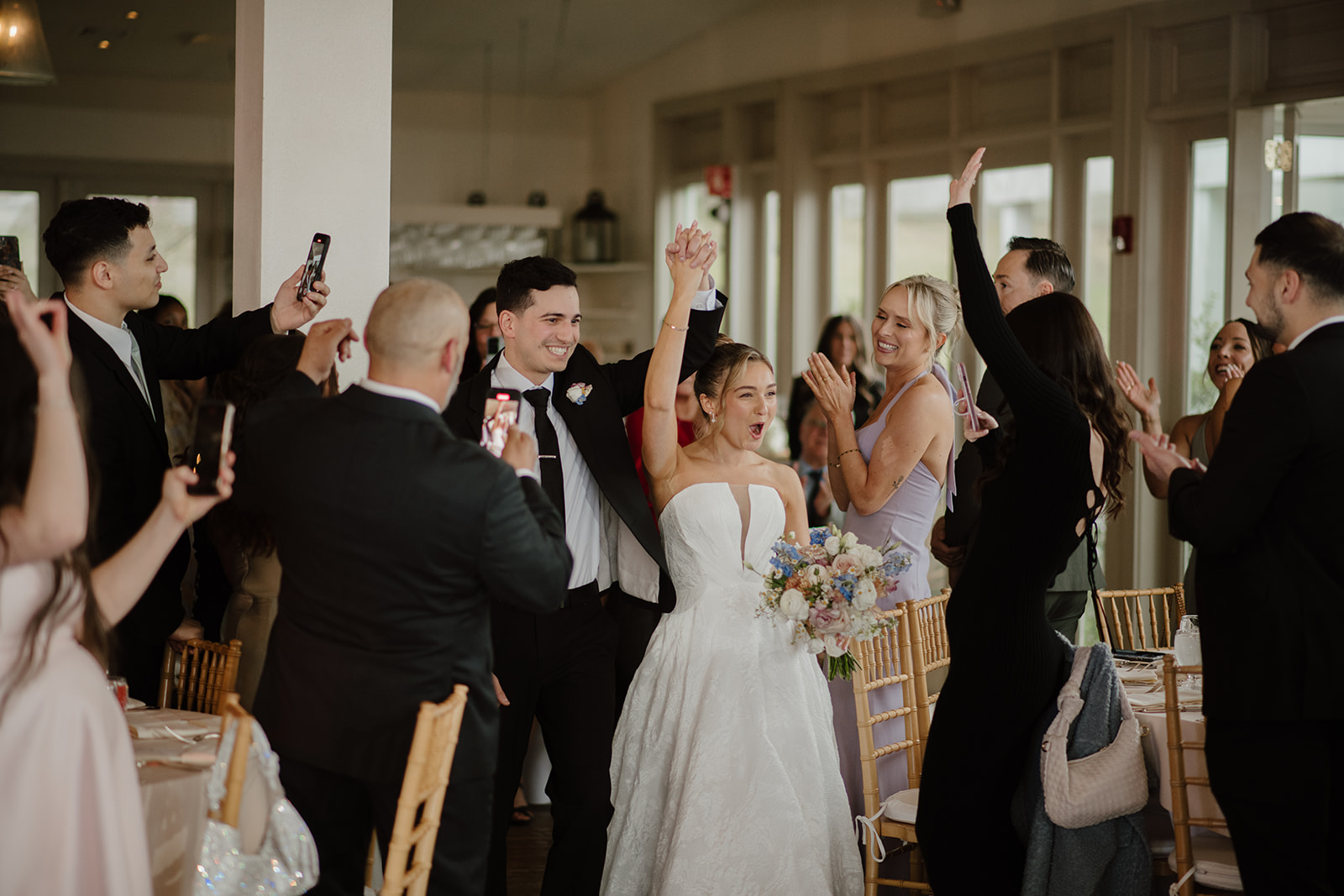 Color photo of the couple's grand entrance into the reception ballroom, holding hands high as guests applaud at The Garrison.