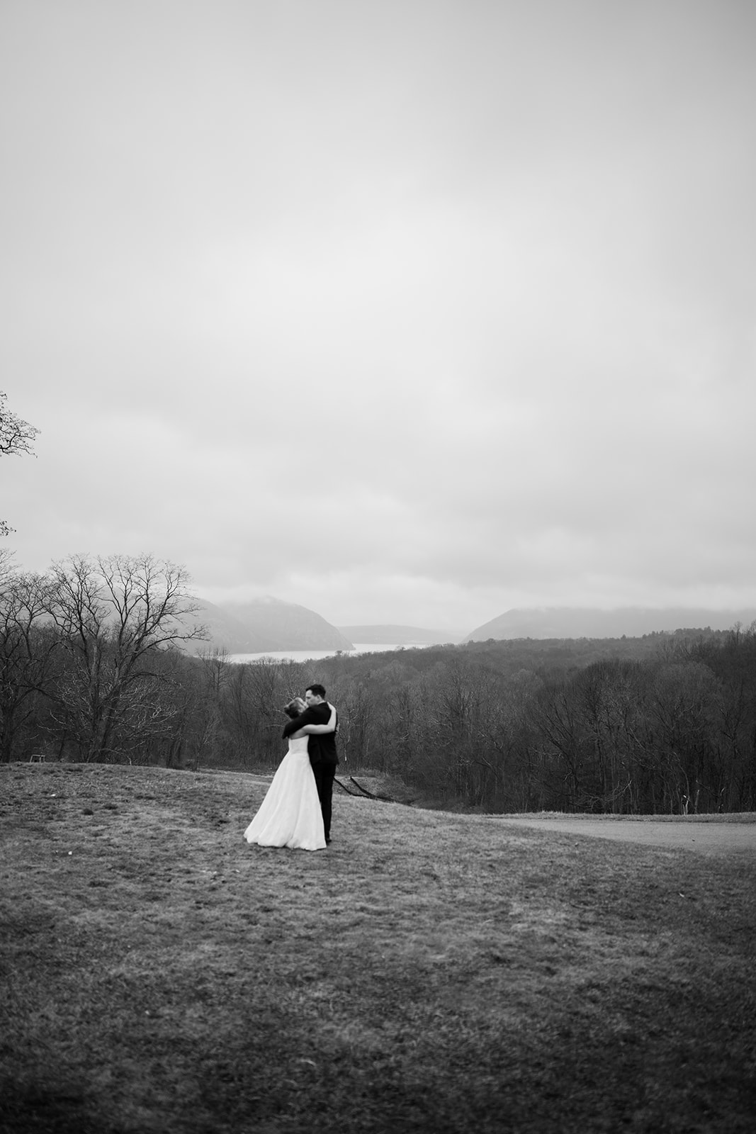 Black and white landscape photo of the bride and groom sharing a quiet embrace on the grassy hillside overlooking the Hudson Valley.