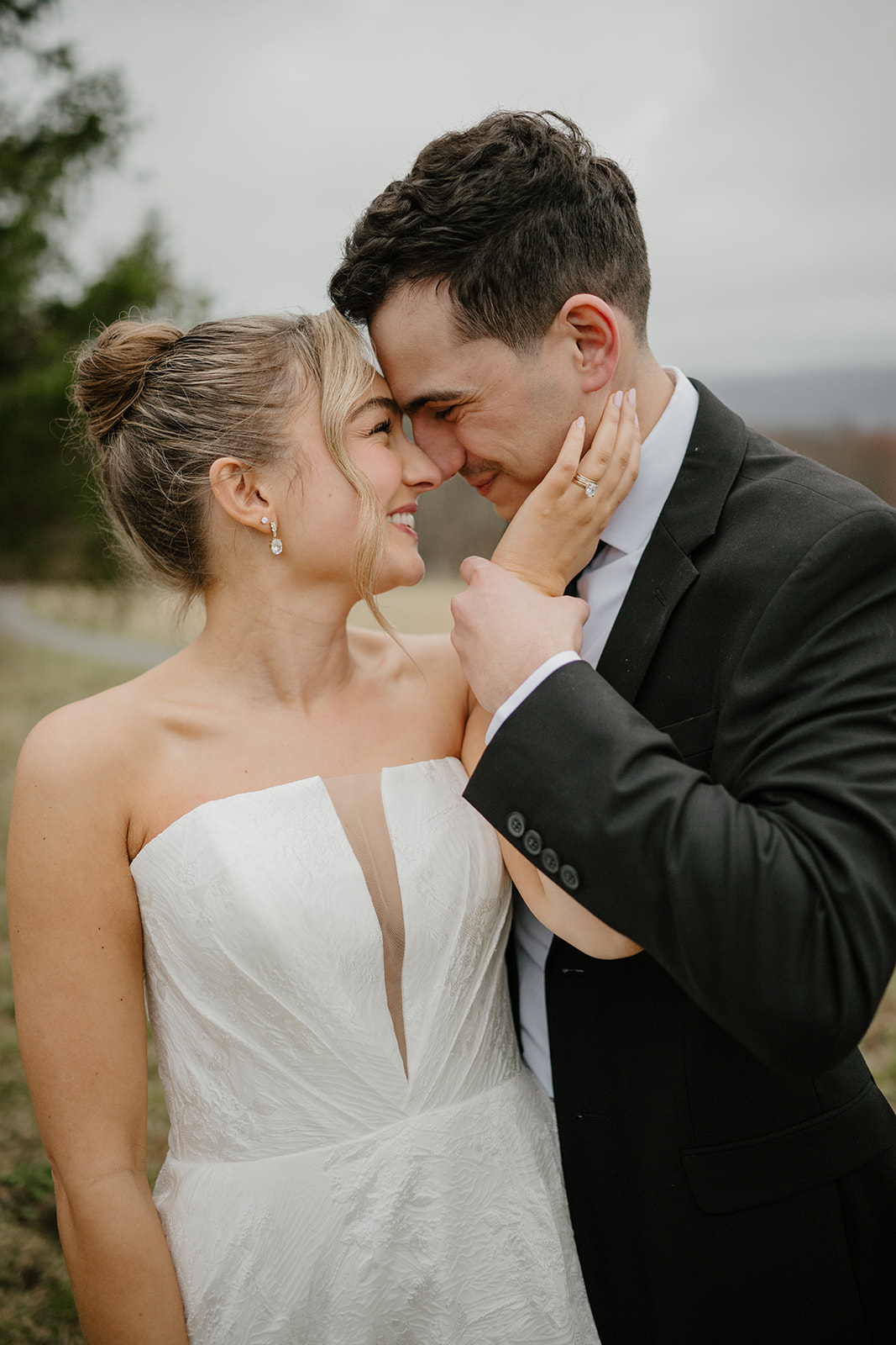 Romantic close-up portrait of the bride and groom nose-to-nose, smiling warmly at each other outdoors.