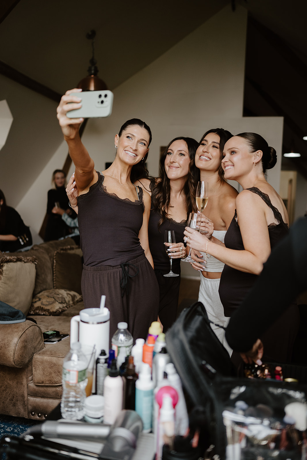 Bride and bridesmaids smile holding champagne glasses as they take a selfie in the dressing room.