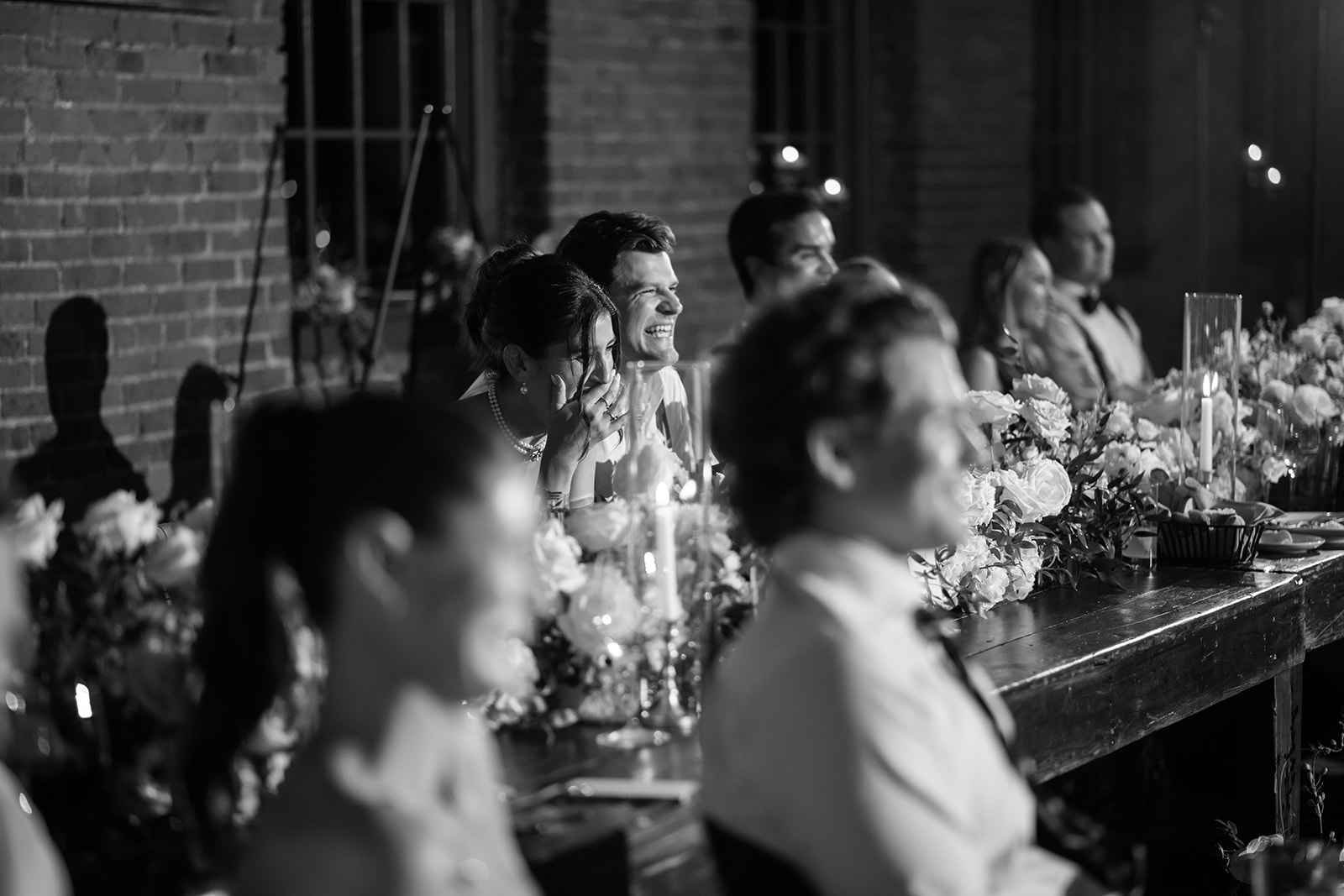 Black and white photo of the bride and groom laughing during wedding toasts at their reception.