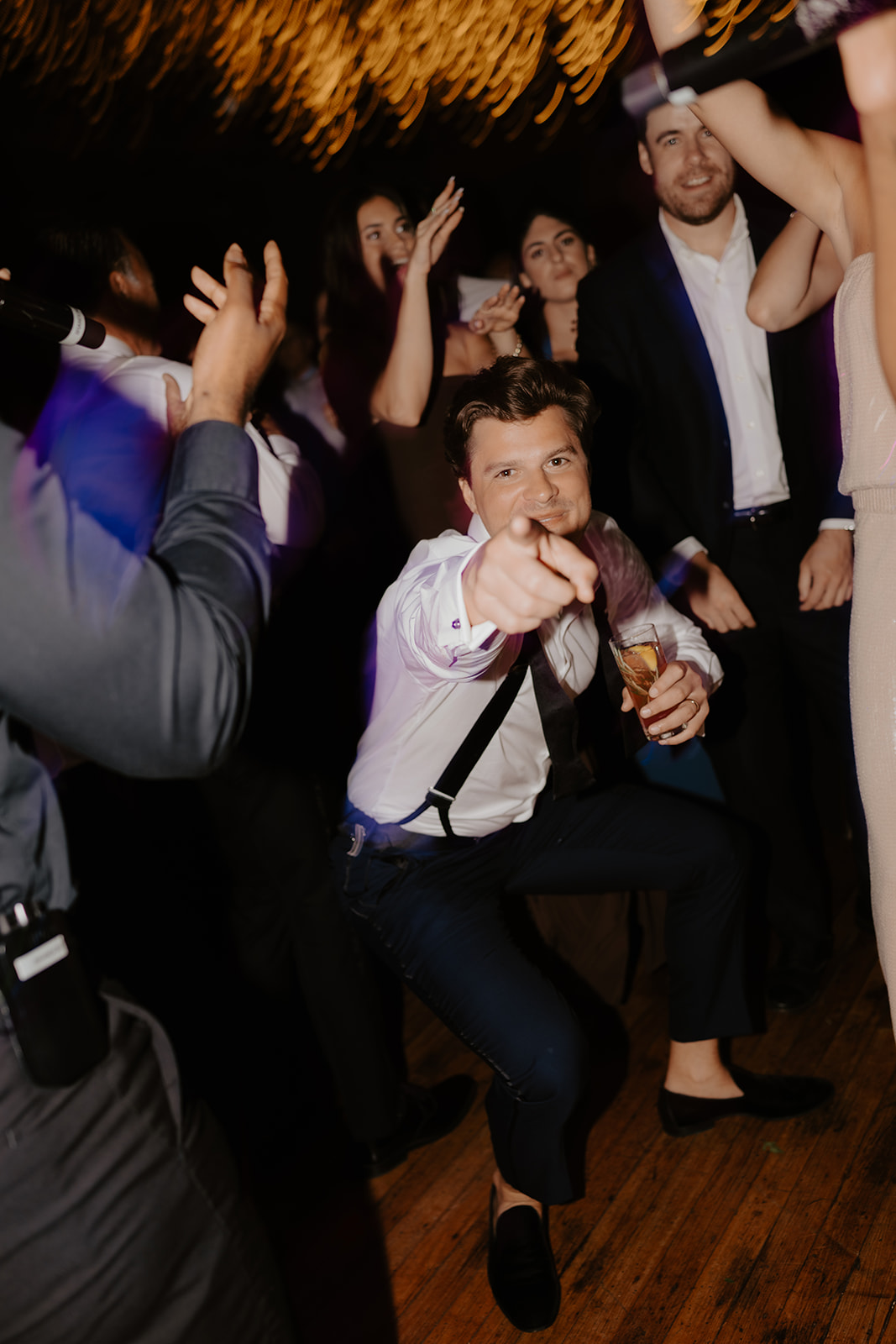 Groom dances energetically and points toward the camera on a lively reception dance floor.
