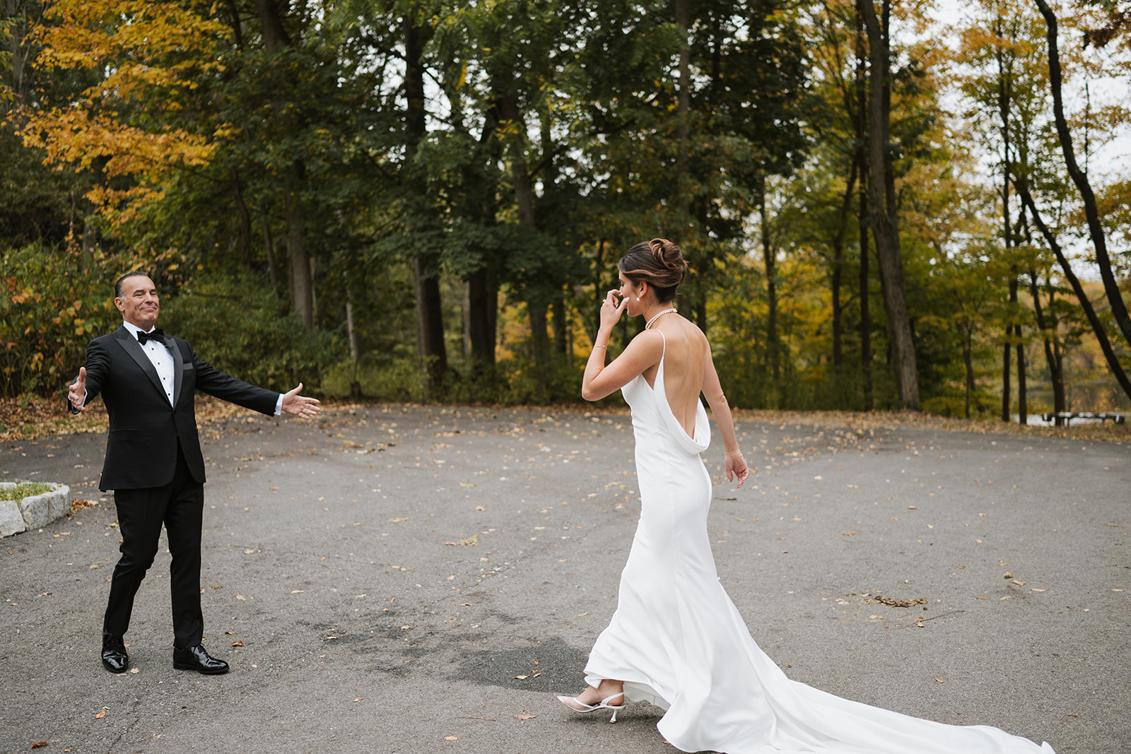 Father of the bride opens his arms in a joyful smile during their outdoor first look.