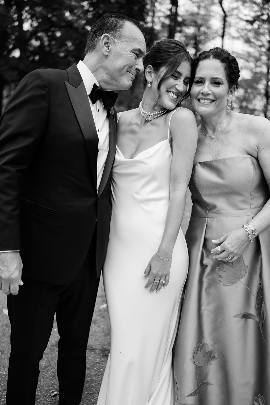 Black and white portrait of the bride laughing with her mother and father outdoors.