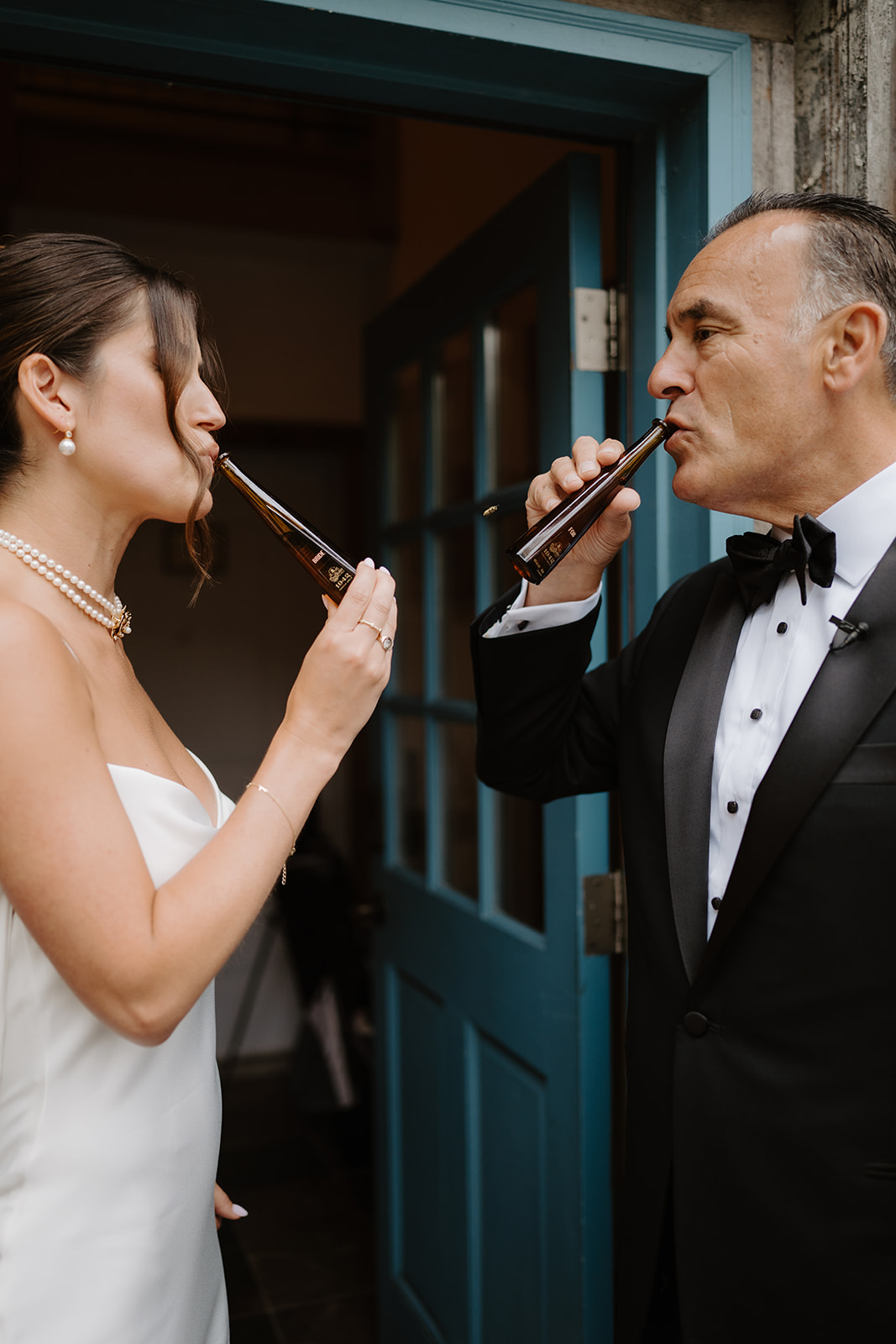 Bride and her father drink miniature shots together in a doorway before the ceremony.