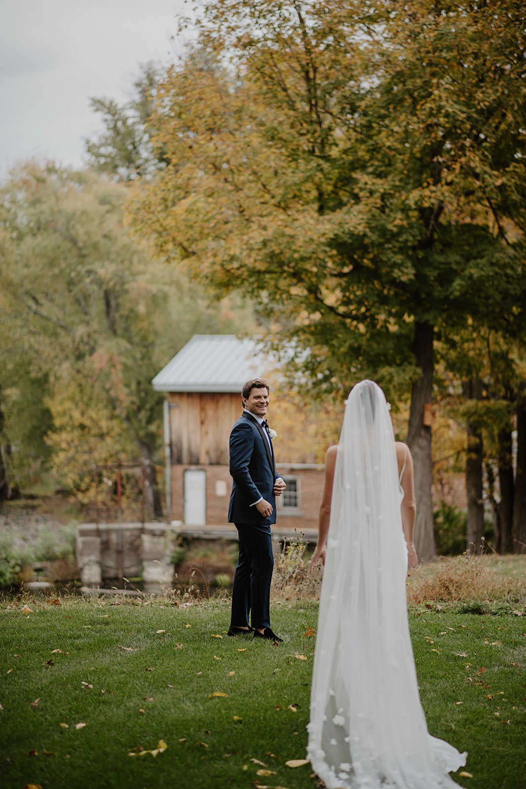 Groom smiles happily as he turns for a first look with his bride in a grassy field.