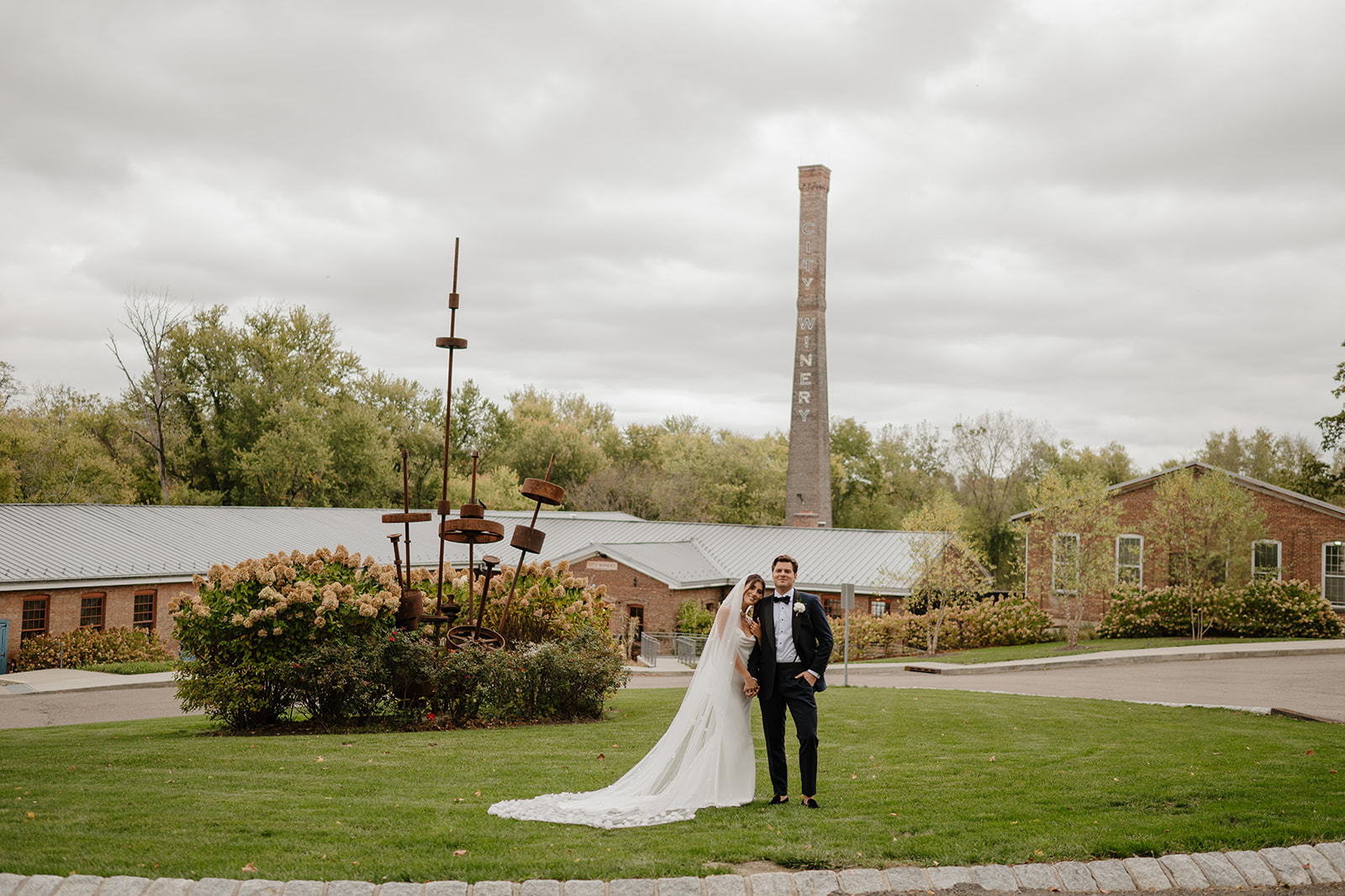 Bride and groom pose on the lawn at City Winery Hudson Valley, with the historic smokestack in the background.