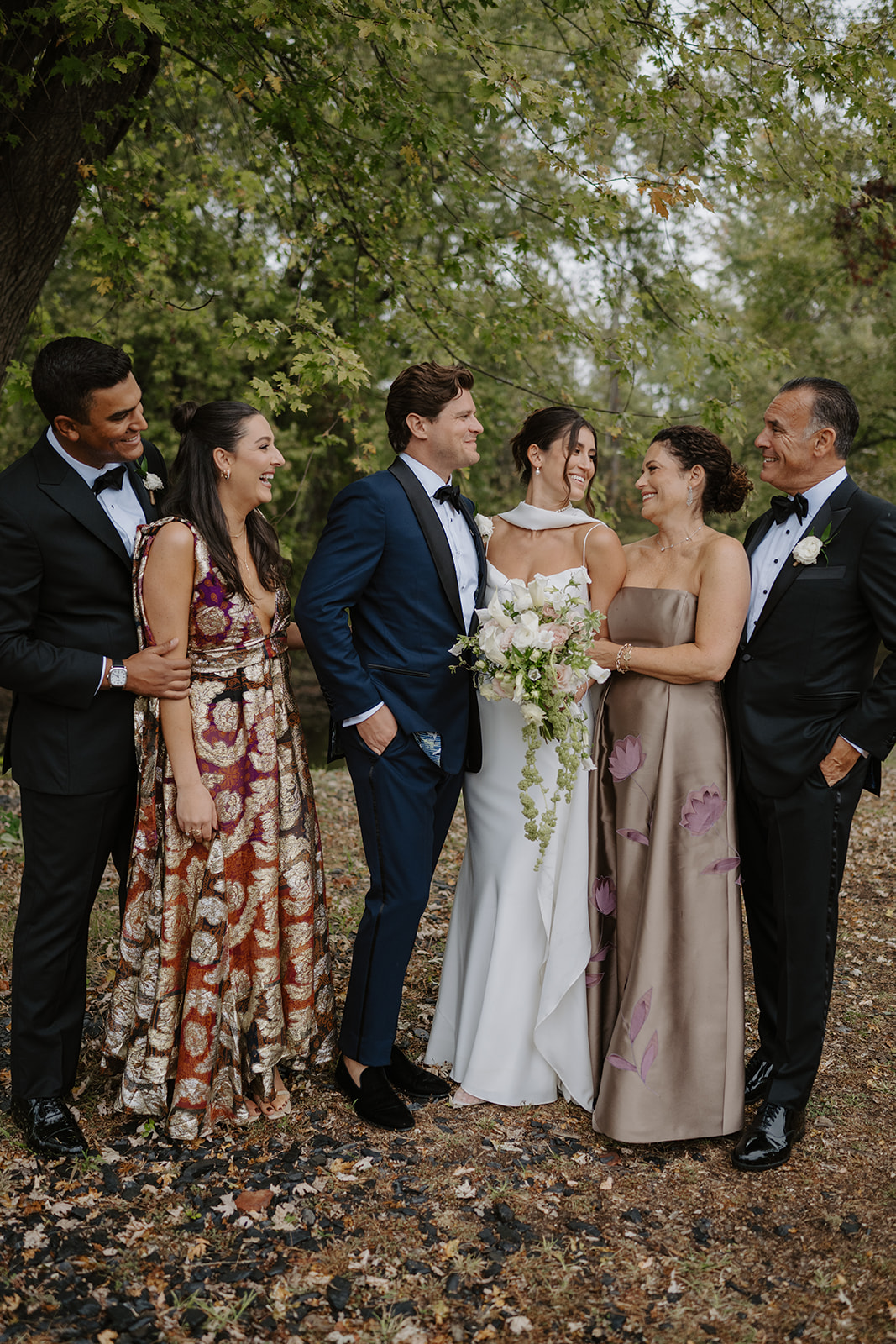 Couple poses with happy family members in stylish gowns and suits under autumn leaves.