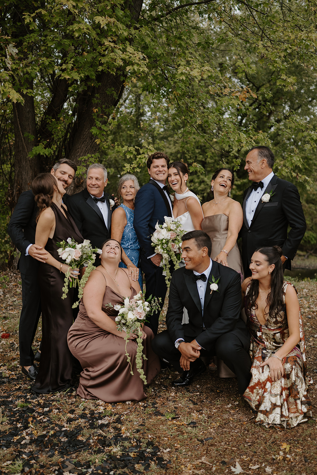 Family members laugh and pose in a playful group portrait under lush green trees.