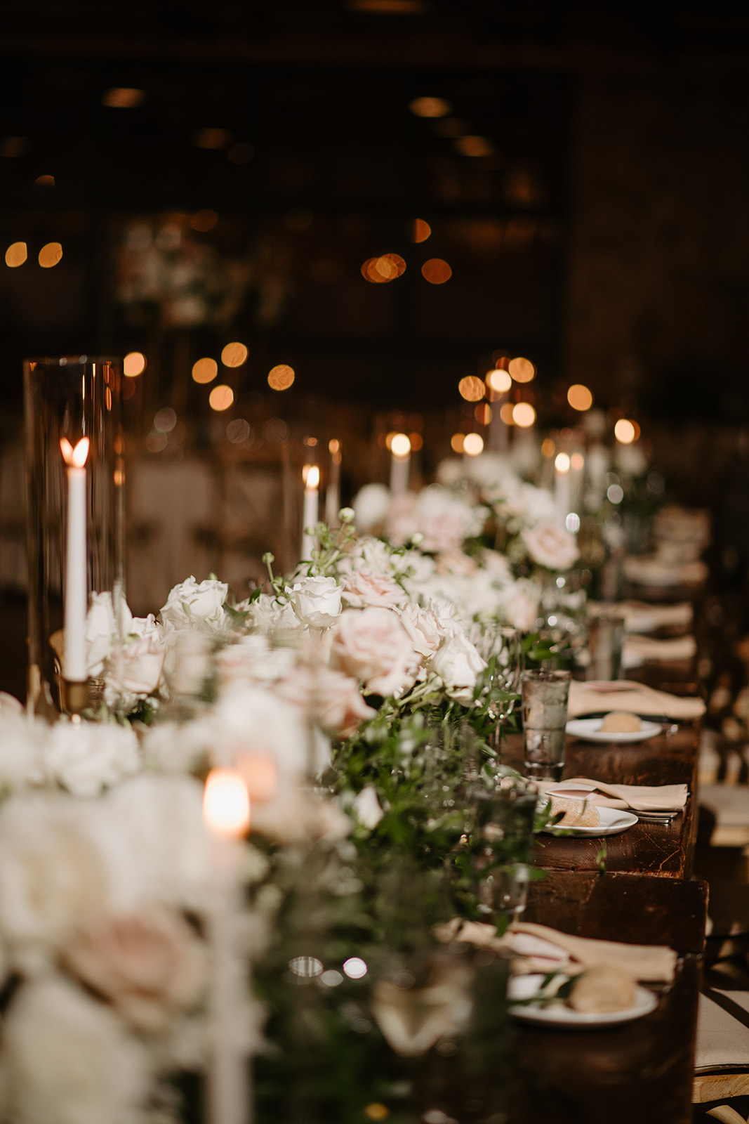 Close-up of elegant white and blush rose centerpieces under warm, ambient candlelight.