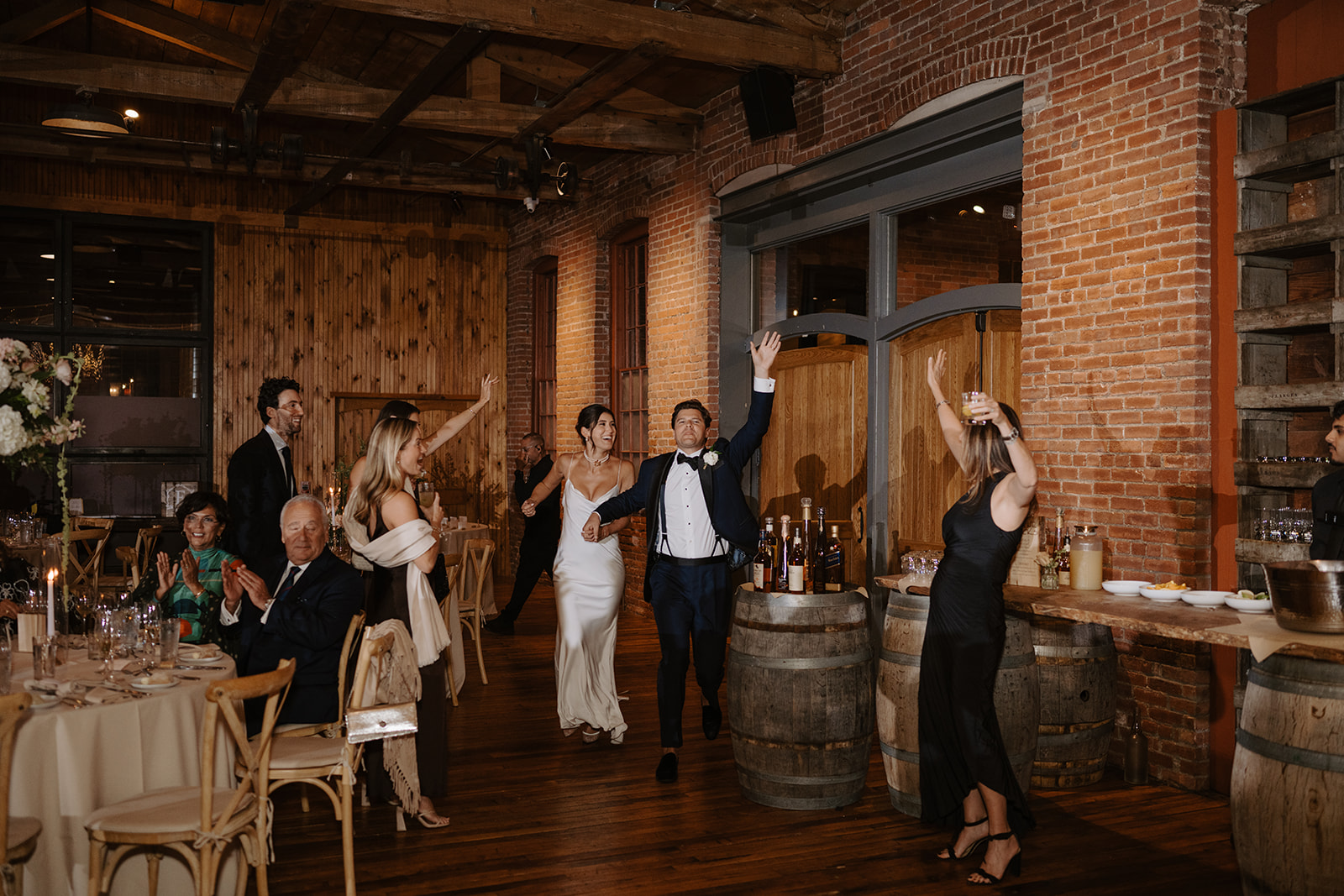Bride and groom make their grand entrance into the reception room, raising their arms as guests cheer.