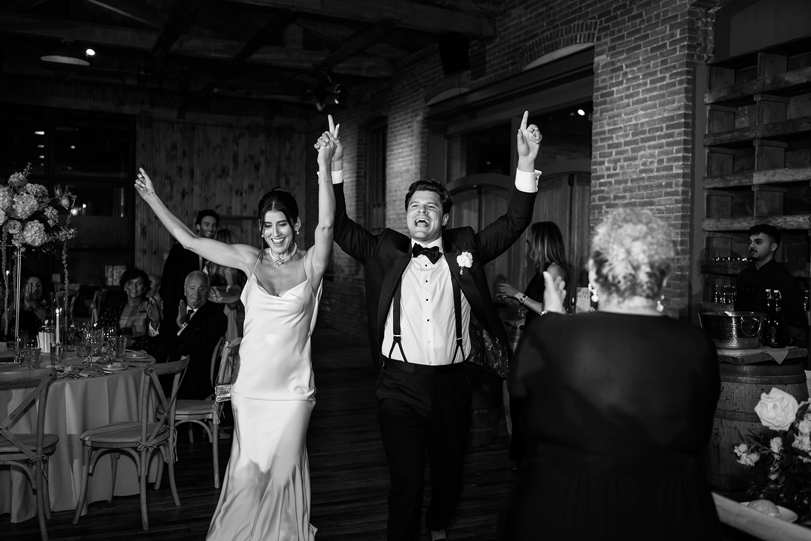 Black and white photo of the bride and groom cheering as they enter their wedding reception.