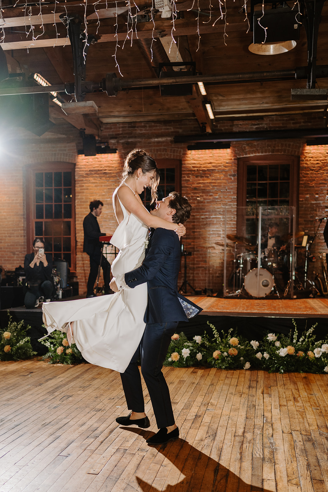 Groom lifts and spins the laughing bride during their first dance on the rustic wooden floor.