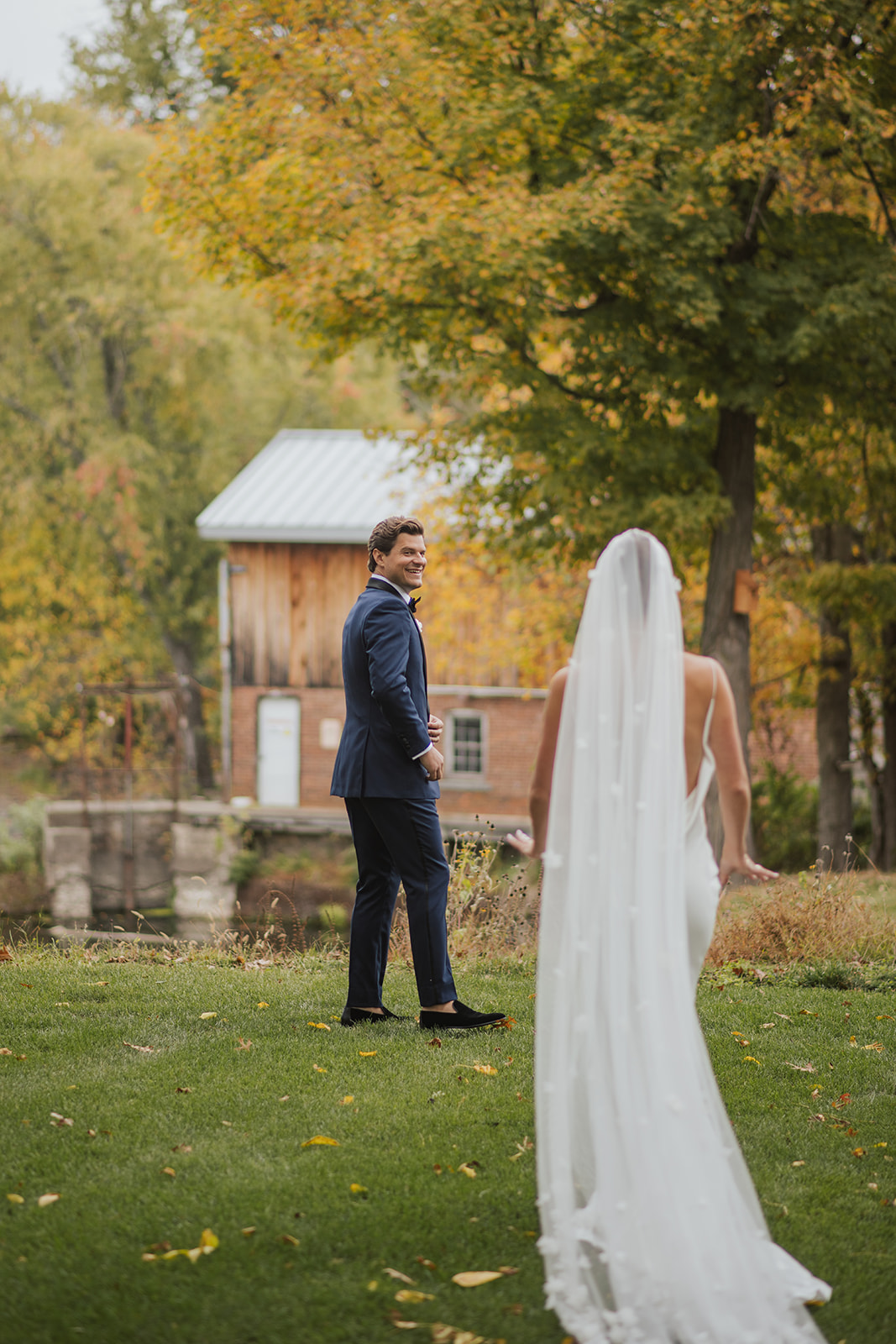 Groom turns with a joyful smile to see his bride during their first look on a grassy field in autumn.