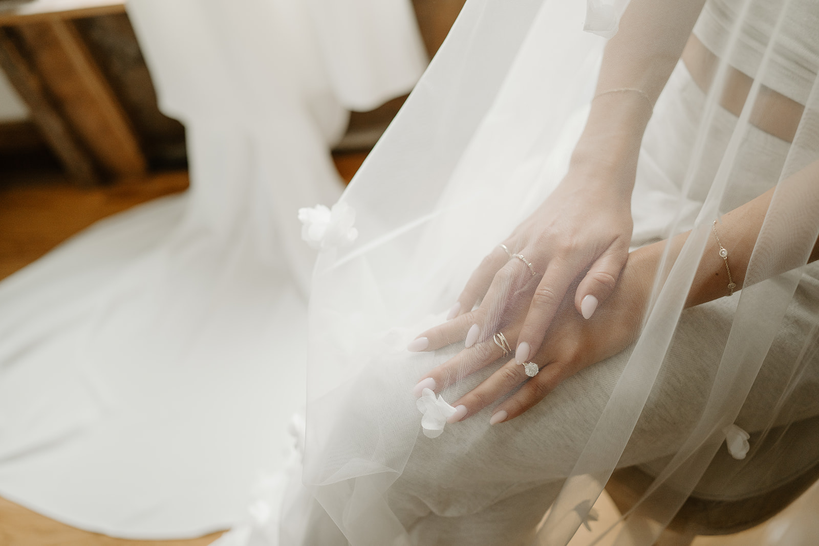 Close-up of the bride's hands with diamond rings resting under a delicate floral veil.