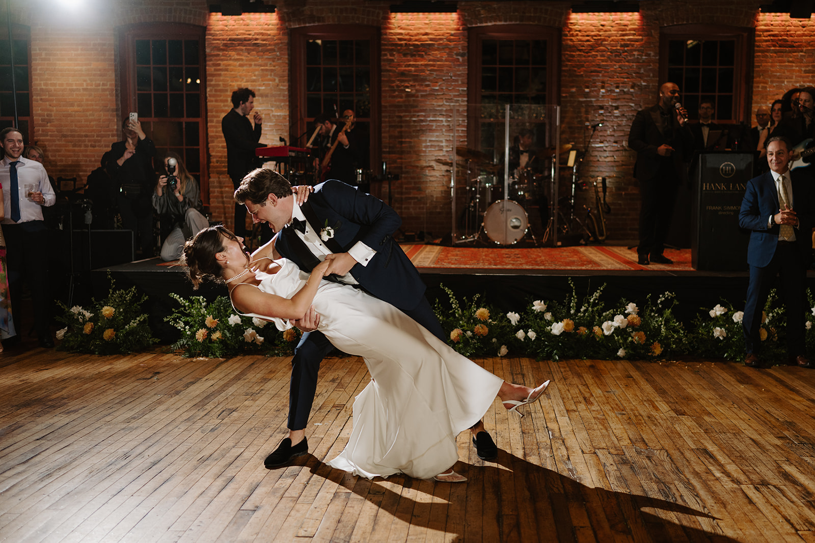 Groom dips the bride during their romantic first dance as a live band plays in the background.
