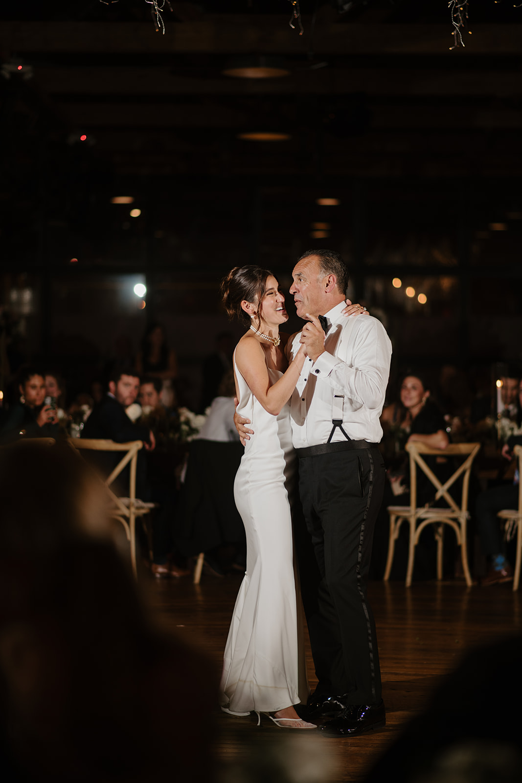 Bride smiles warmly while sharing a dance with her father during the reception.