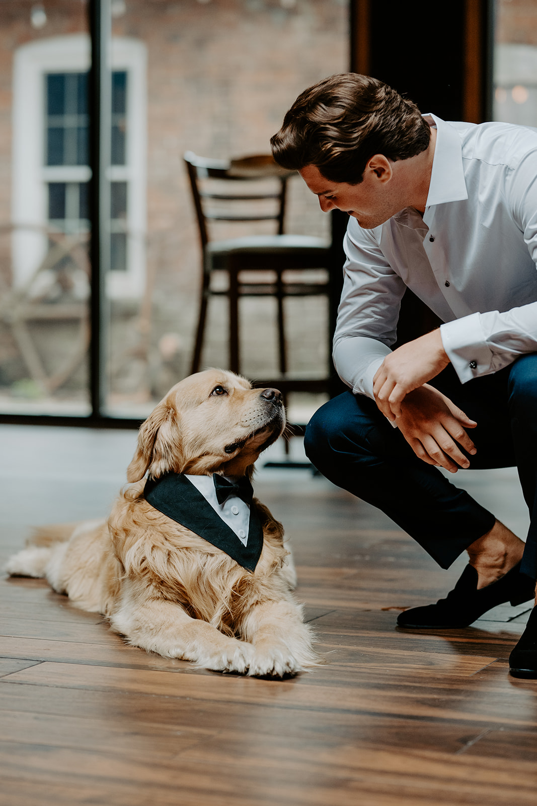 Groom smiles lovingly at his golden retriever wearing a tuxedo bandana before the ceremony.