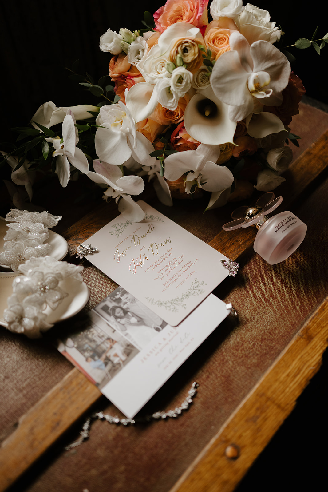 Peach and white bridal bouquet resting beside the invitation suite and pearls on a wooden table.