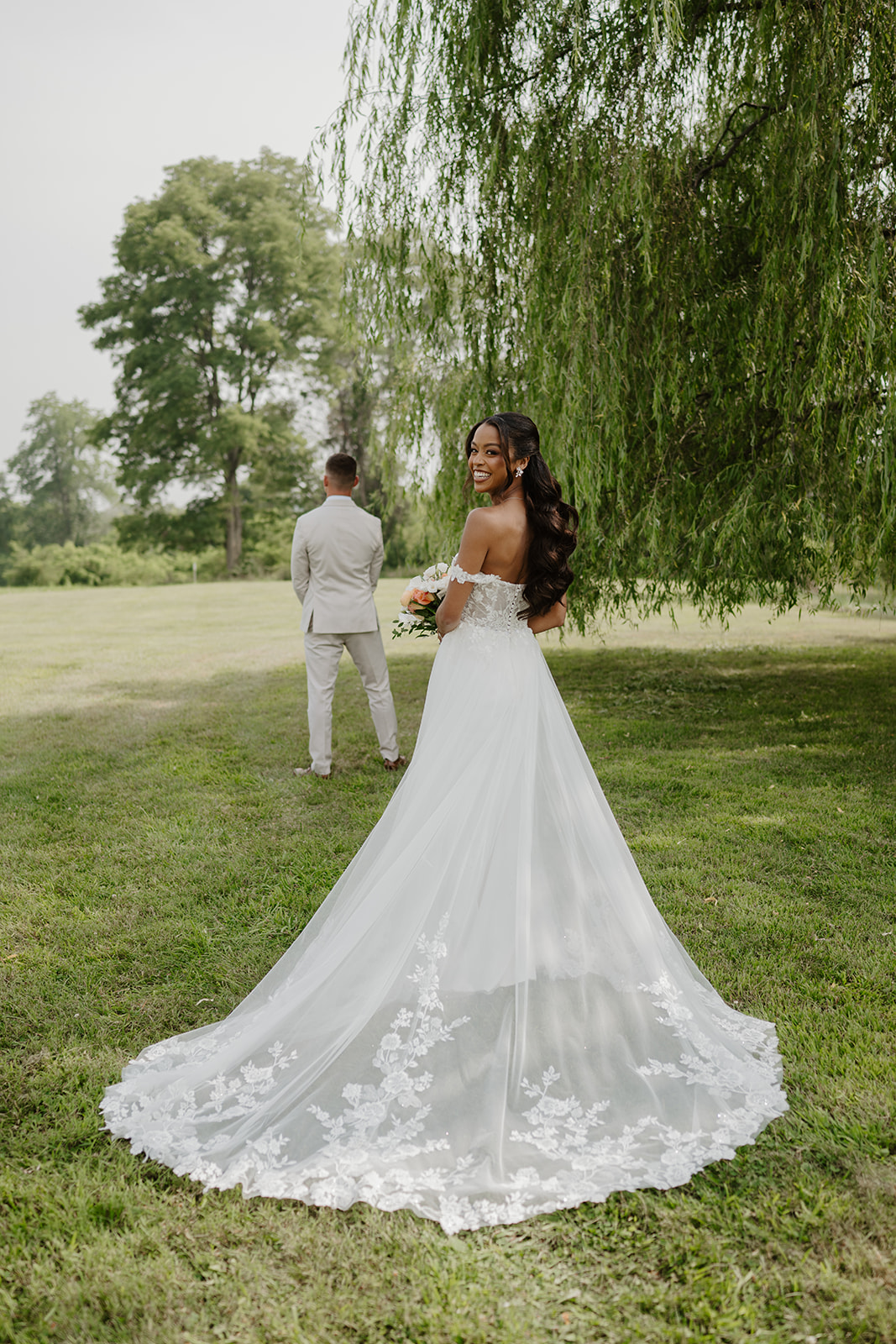 Bride looking back over her shoulder beneath the willow tree before her first look at Red Maple Vineyard, West Park NY