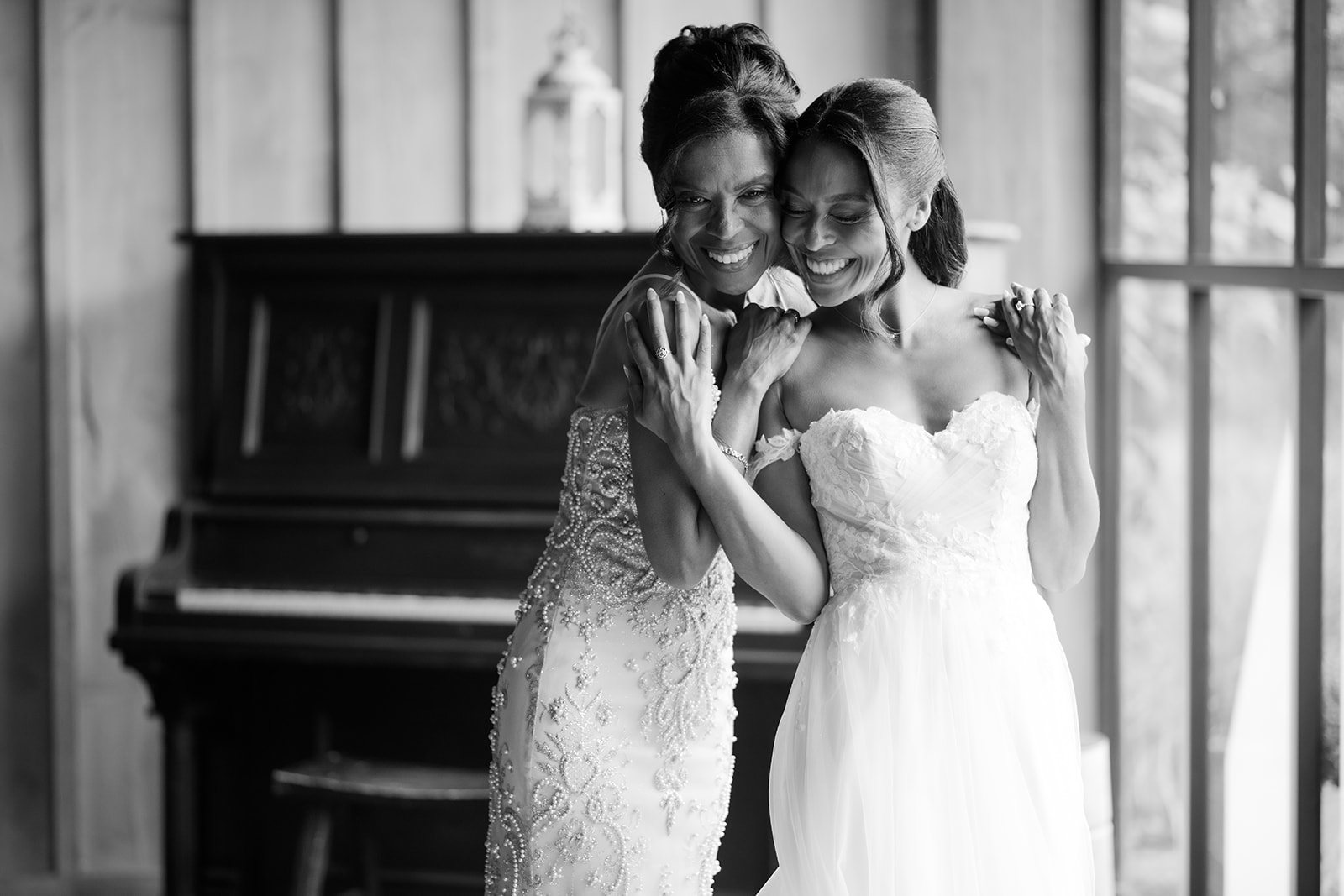 Black and white photo of the bride and a bridesmaid smiling beside the antique piano.