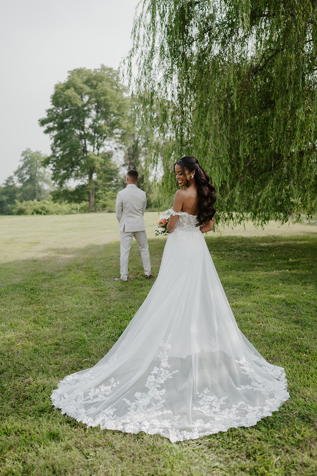 Bride turns to look back at the groom beneath the willow tree.
