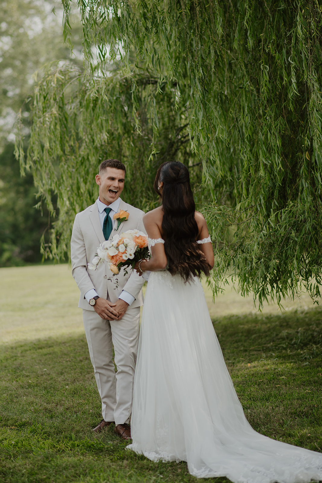 Groom smiles at the bride as they stand together under the willow branches.