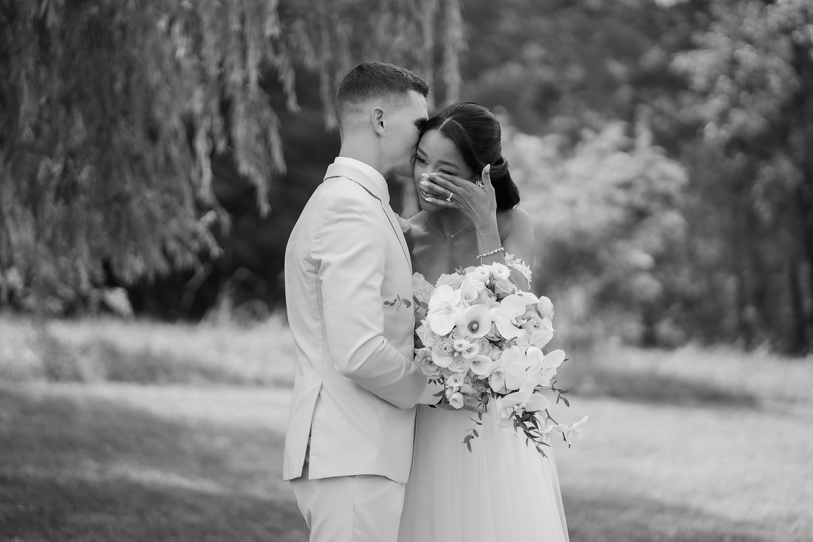 Black and white photo of the couple laughing forehead to forehead with her bouquet raised.