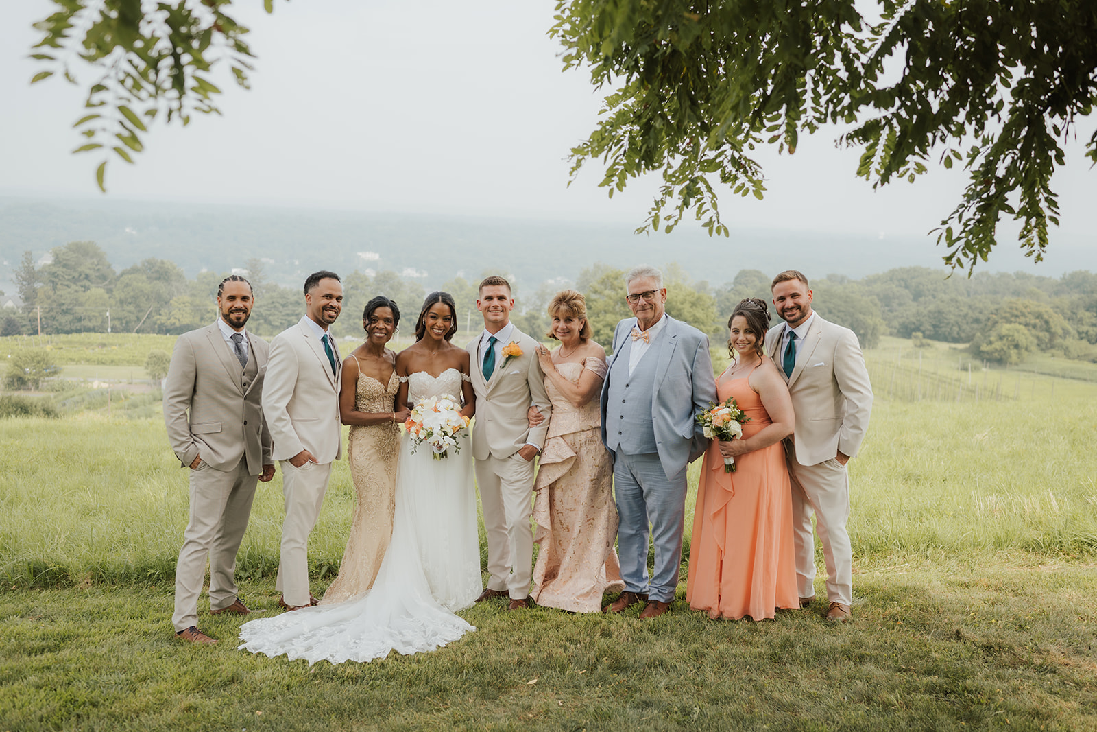 Bride and groom pose with their bridal party and family on the hillside.