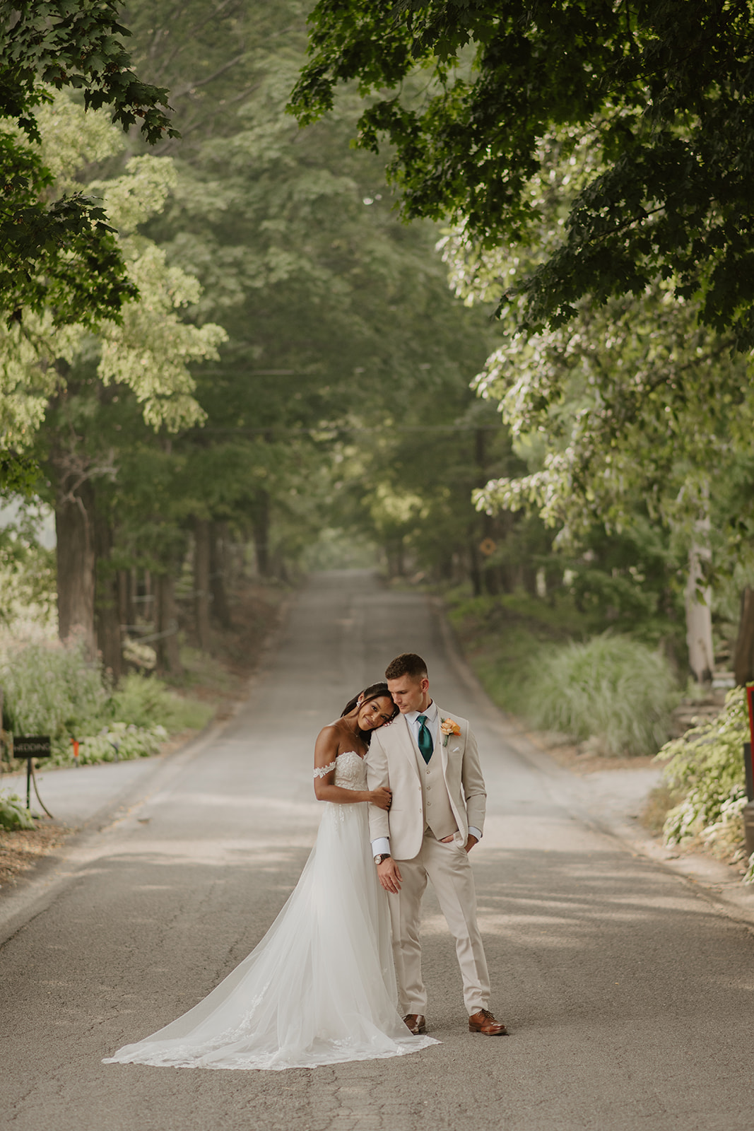 Bride and groom stand close on the tree-lined country road at the vineyard.