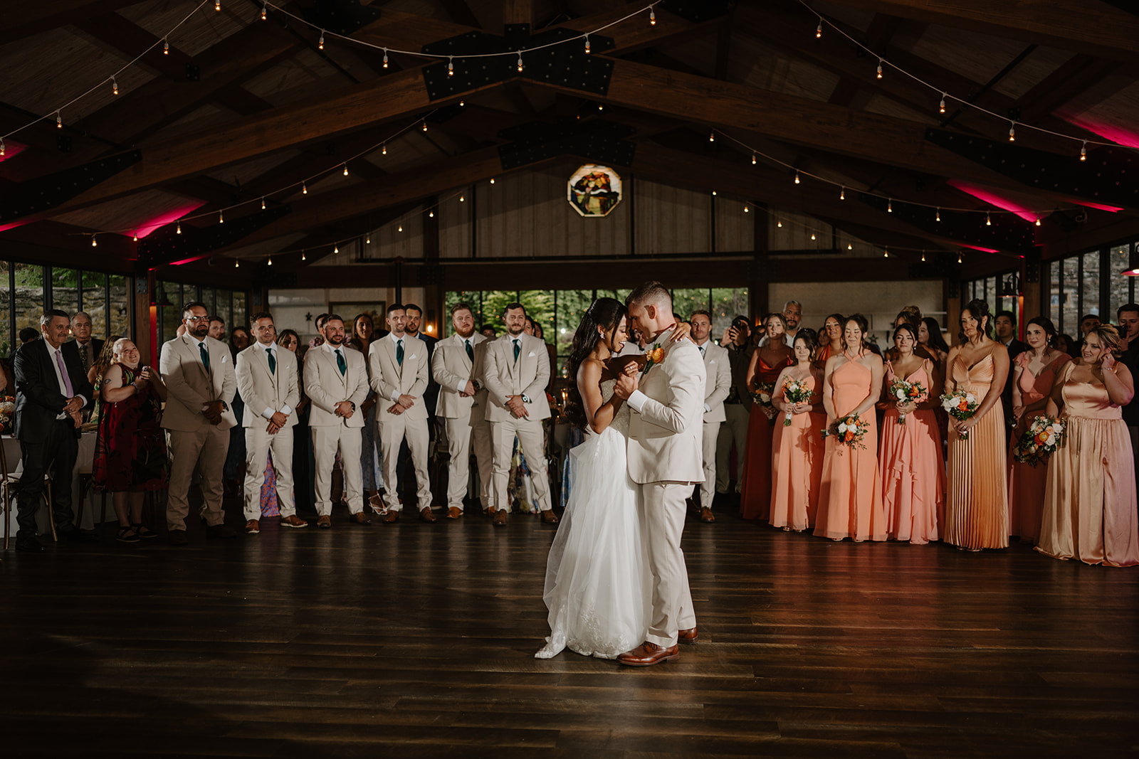 Bride and groom share their first dance as the bridal party looks on.