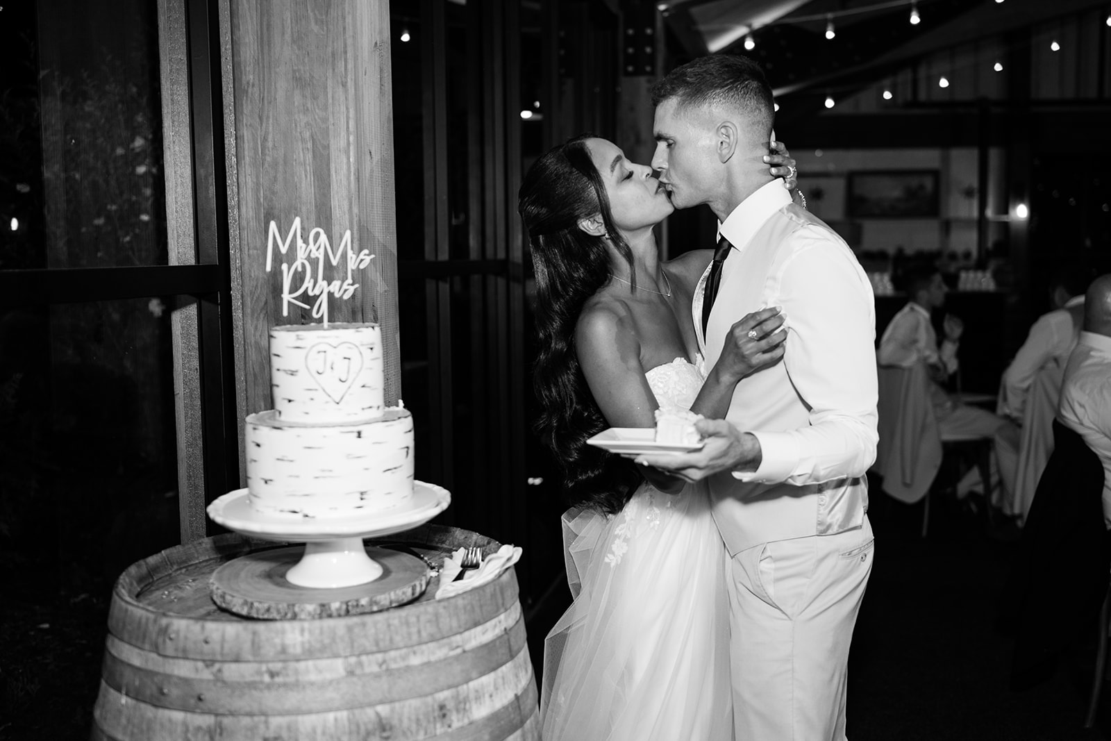 Black and white photo of the newlyweds sharing a kiss after cutting their wedding cake.