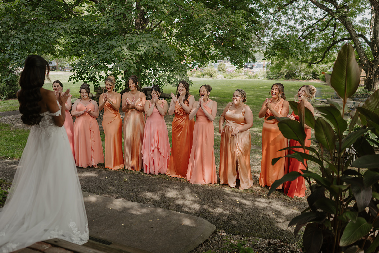 Bride greets her bridesmaids in coral gowns lined up along the garden path.