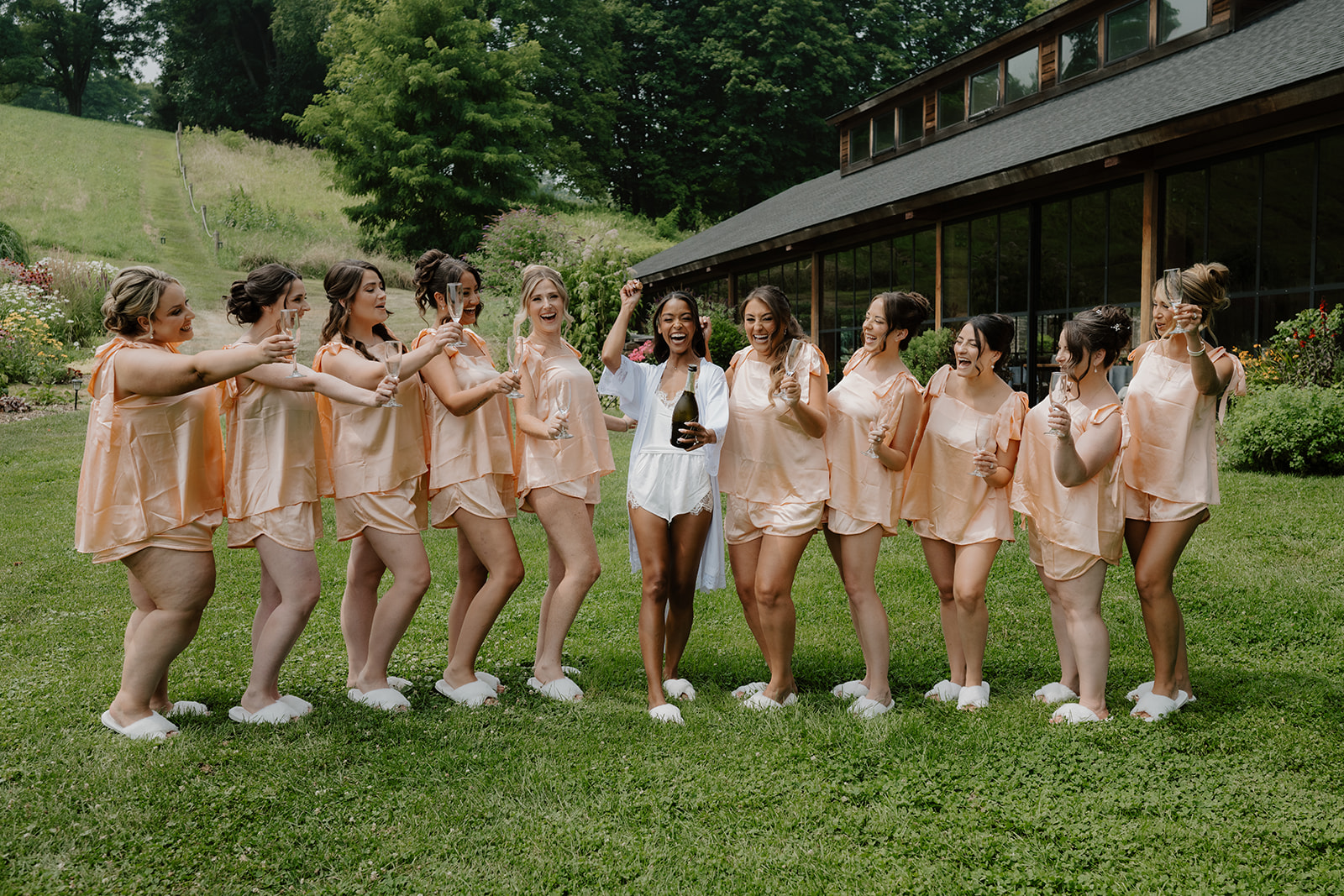 Bridesmaids in peach pajamas dance across the lawn outside the barn.