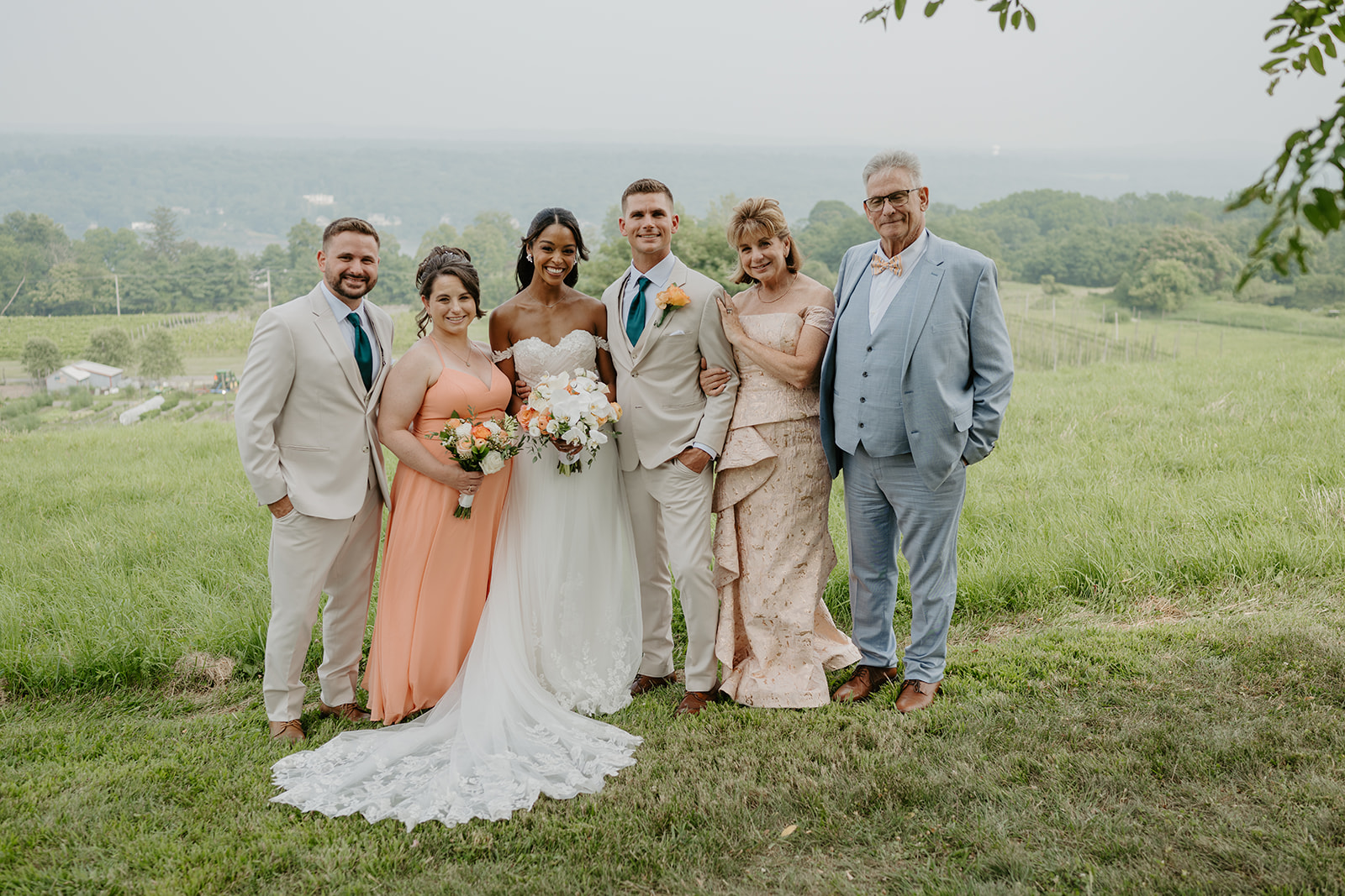Bride and groom smile with family members on the green hillside.