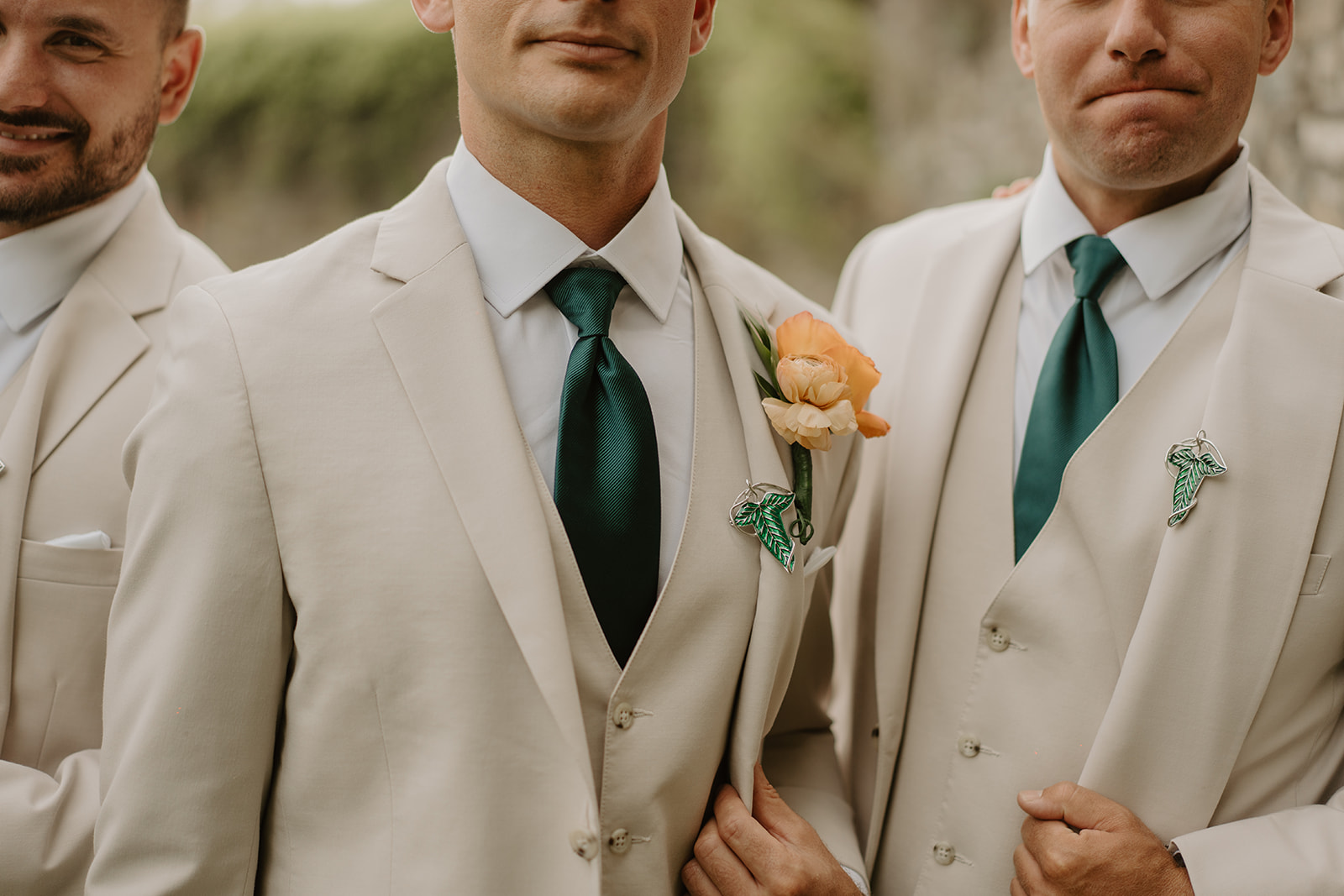 Groomsmen in cream suits and deep green ties stand shoulder to shoulder.