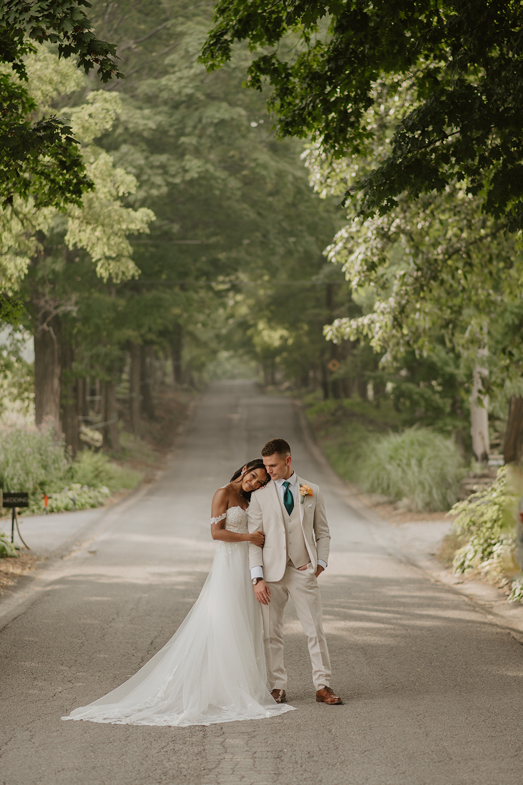 Bride and groom embrace on a tree-lined lane, her train sweeping the ground.