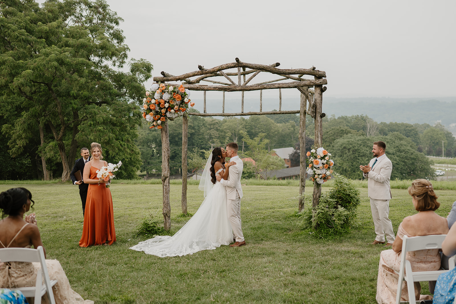 Bride walks down the aisle toward the floral arch as guests look on.
